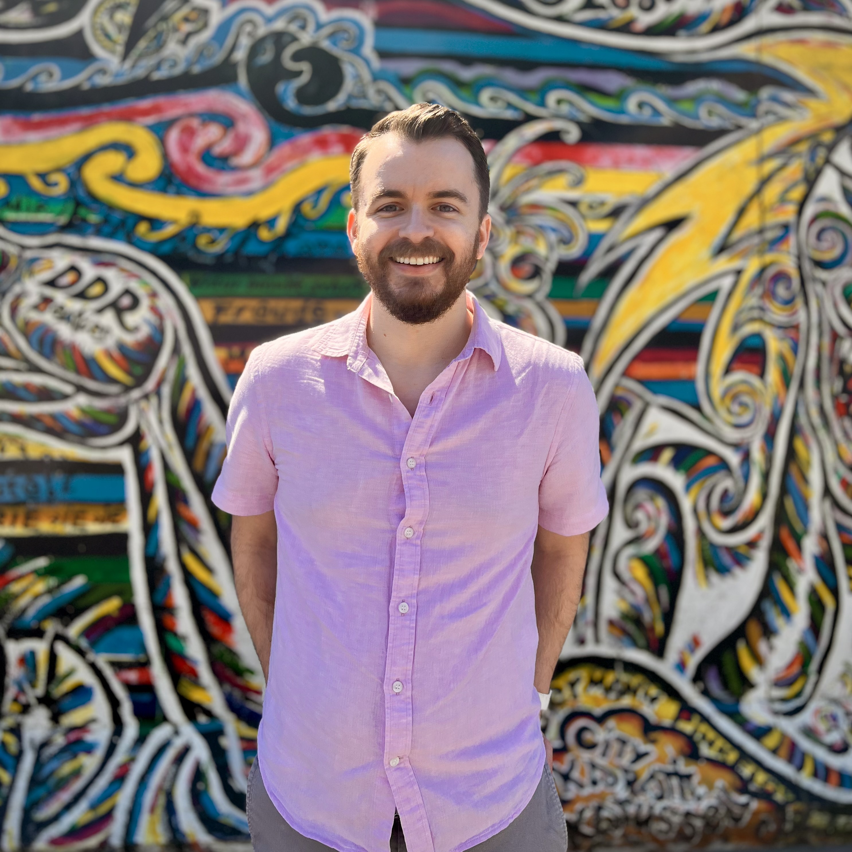 Andrew Grojean standing in front of colorful Berlin Wall artwork.